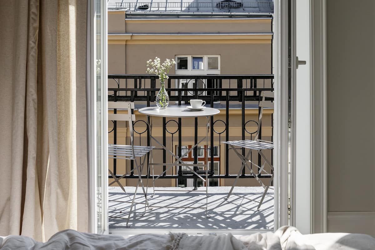 An open balcony with a view of a building's roof and a table with chairs.