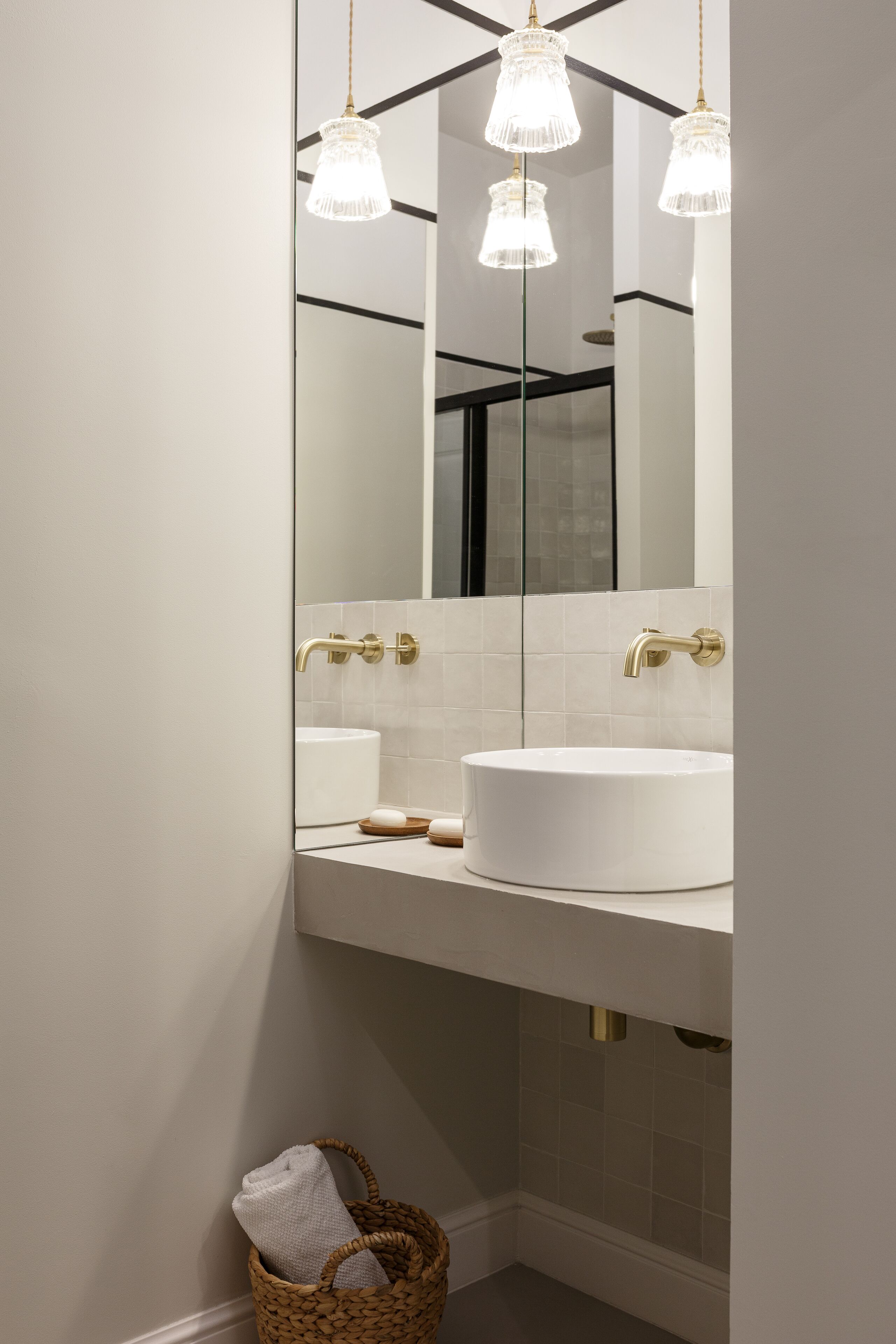 A modern bathroom with a large mirror, a white sink, gold fixtures, and three hanging lights.