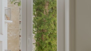 A room with a window overlooking a garden, a chair, and a table with a book and a vase. - Lwowska Studios - STAYINWARSAW (Warsaw)