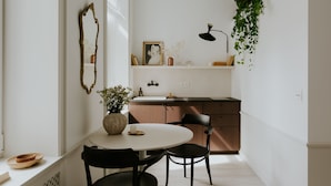 A dining area with a round table, two chairs, a vase with flowers, and a mirror on the wall. - Lwowska Studios - STAYINWARSAW (Warsaw)