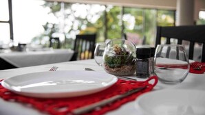 Une table à manger avec une assiette blanche, une serviette rouge et un petit bol en verre contenant une plante.