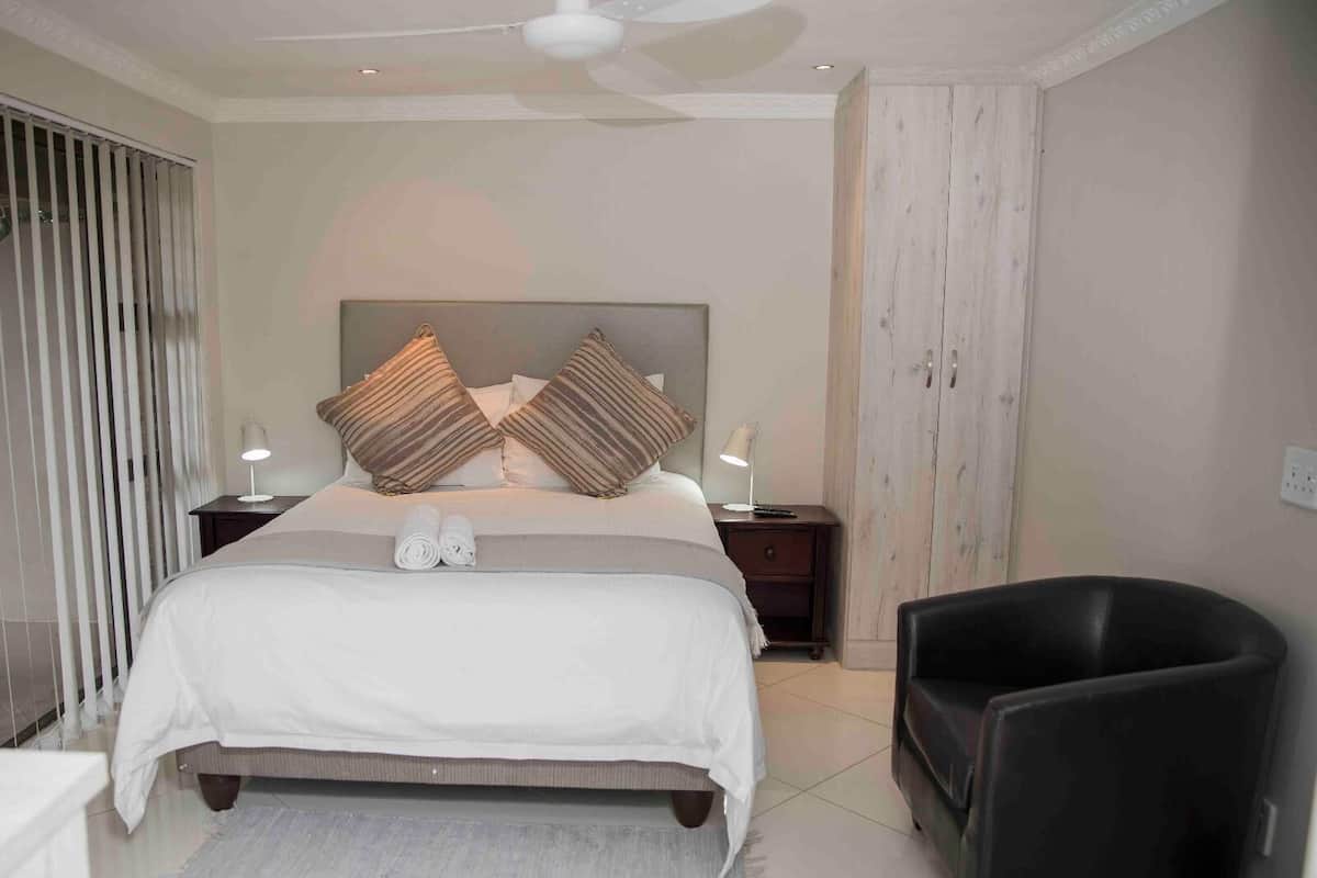 Une chambre à coucher comprenant un lit, deux tables de chevet avec des lampes, une chaise, une armoire et un ventilateur de plafond.