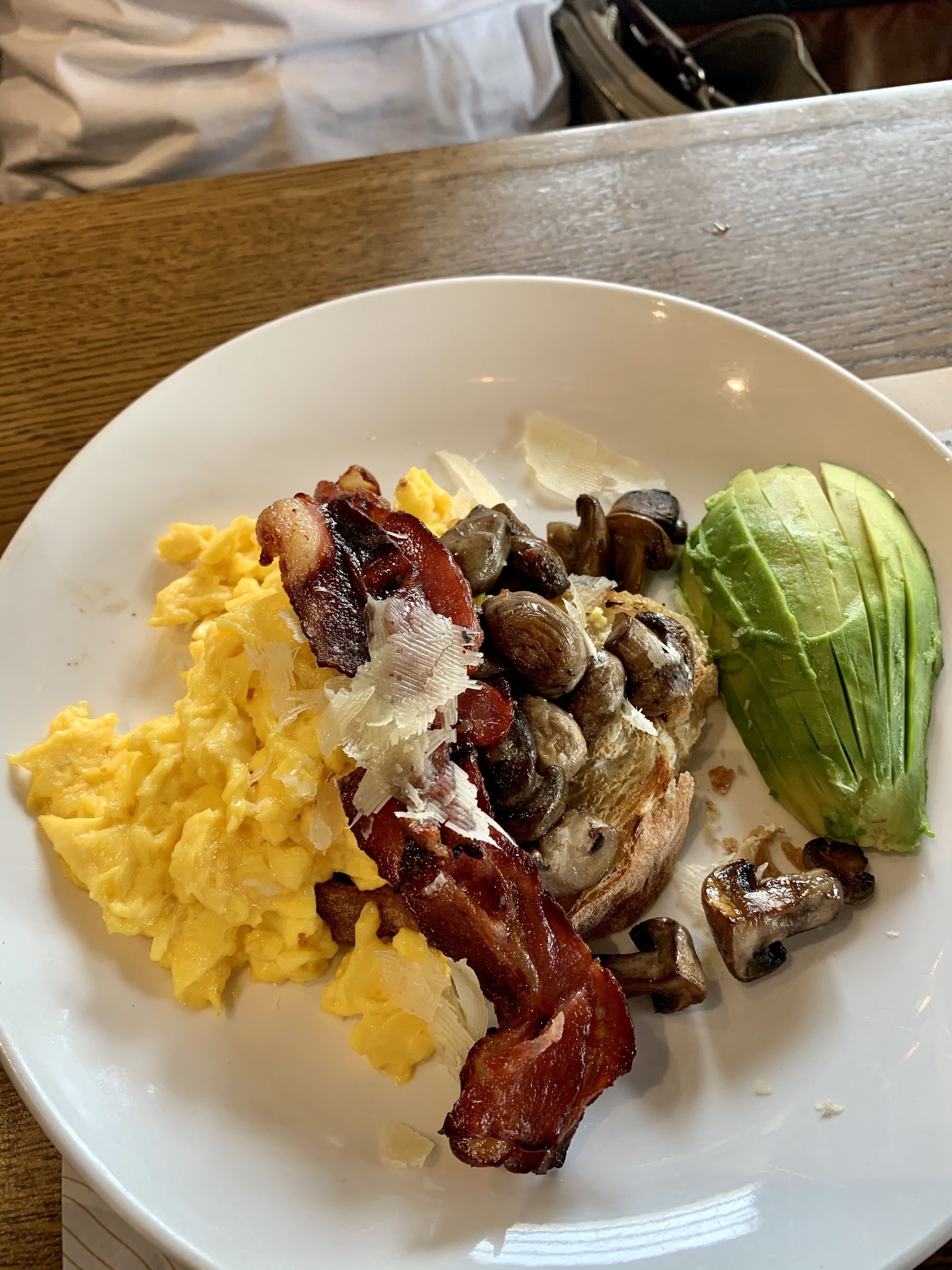 A plate with scrambled eggs, bacon, mushrooms, and avocado.