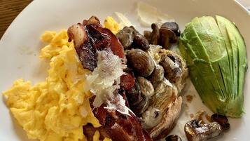 A plate with scrambled eggs, bacon, mushrooms, and avocado.