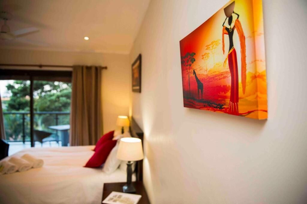 Quarto de hotel com cama, mesa de cabeceira, abajur e um quadro na parede.