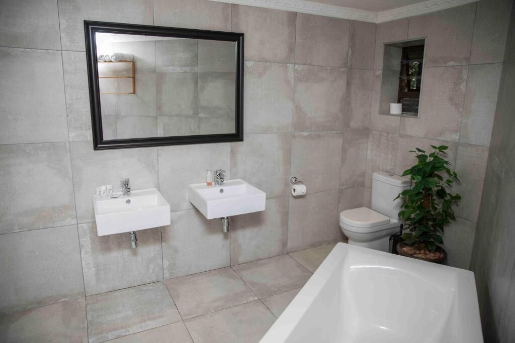 A bathroom with two sinks, a toilet, a bathtub, a mirror, and a potted plant.