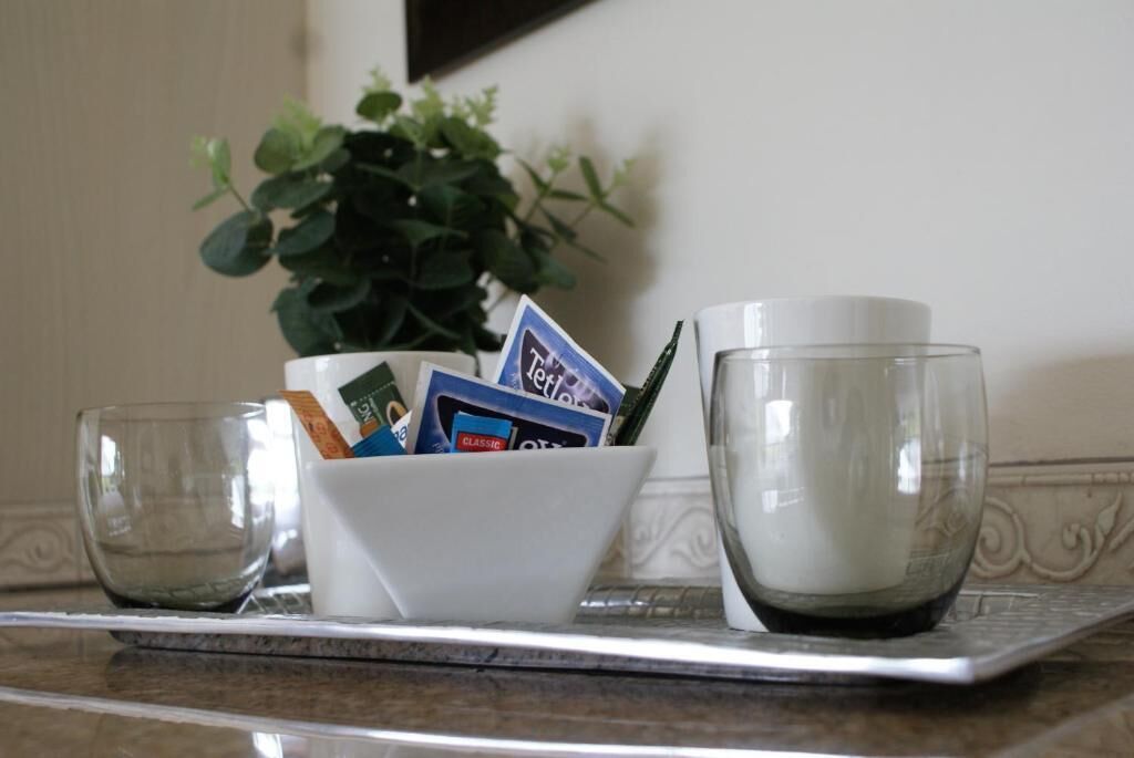 Una bandeja con un tazón blanco que contiene varios objetos, incluyendo una taza blanca y un vaso transparente.
