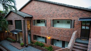 Un immeuble en briques à plusieurs étages, doté d’un patio couvert, d’un escalier et d’un petit jardin.