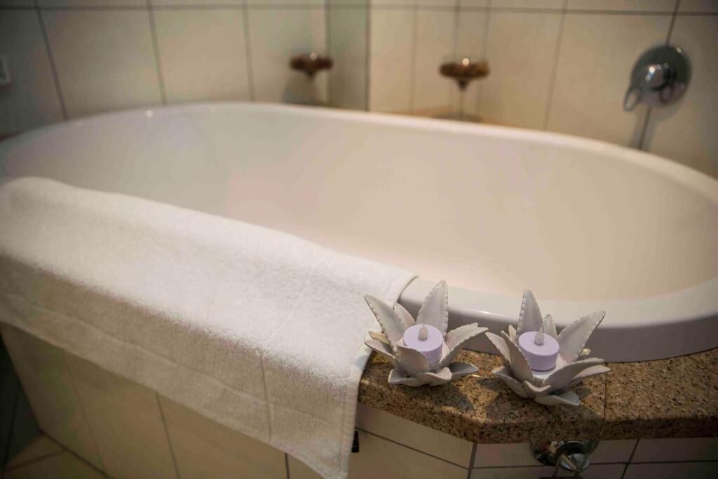 A bathtub with a white towel, two decorative candles, and a granite countertop.
