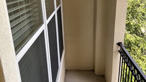 A narrow balcony with a black metal railing, beige walls, and a window with blinds.
