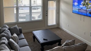 A living room with a sofa, a coffee table, and a TV mounted on the wall.