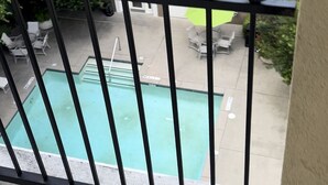 A view of a swimming pool from a balcony with a metal railing.