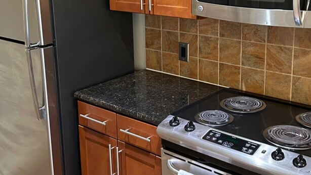 A kitchen with wooden cabinets, a stainless steel refrigerator, a microwave, and a stove.