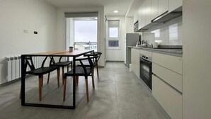 A modern kitchen with a dining area, featuring a central island with chairs, a built-in oven, and a view to the outside. - Jainen Apartamentos (Ushuaia)