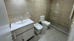 A modern bathroom with a glass shower enclosure, a white sink, and a bidet. - Jainen Apartamentos (Ushuaia)