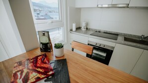 A kitchen with white cabinets, a wooden table, a potted plant, and a coffee maker. - Jainen Apartamentos (Ushuaia)