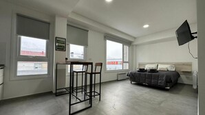 A modern bedroom with a bed, a desk, and two chairs. There are large windows and a mounted TV. - Jainen Apartamentos (Ushuaia)