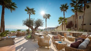 An outdoor patio with wicker furniture, palm trees, and a view of the sea. - Mirari Boutique Hotel (Split)