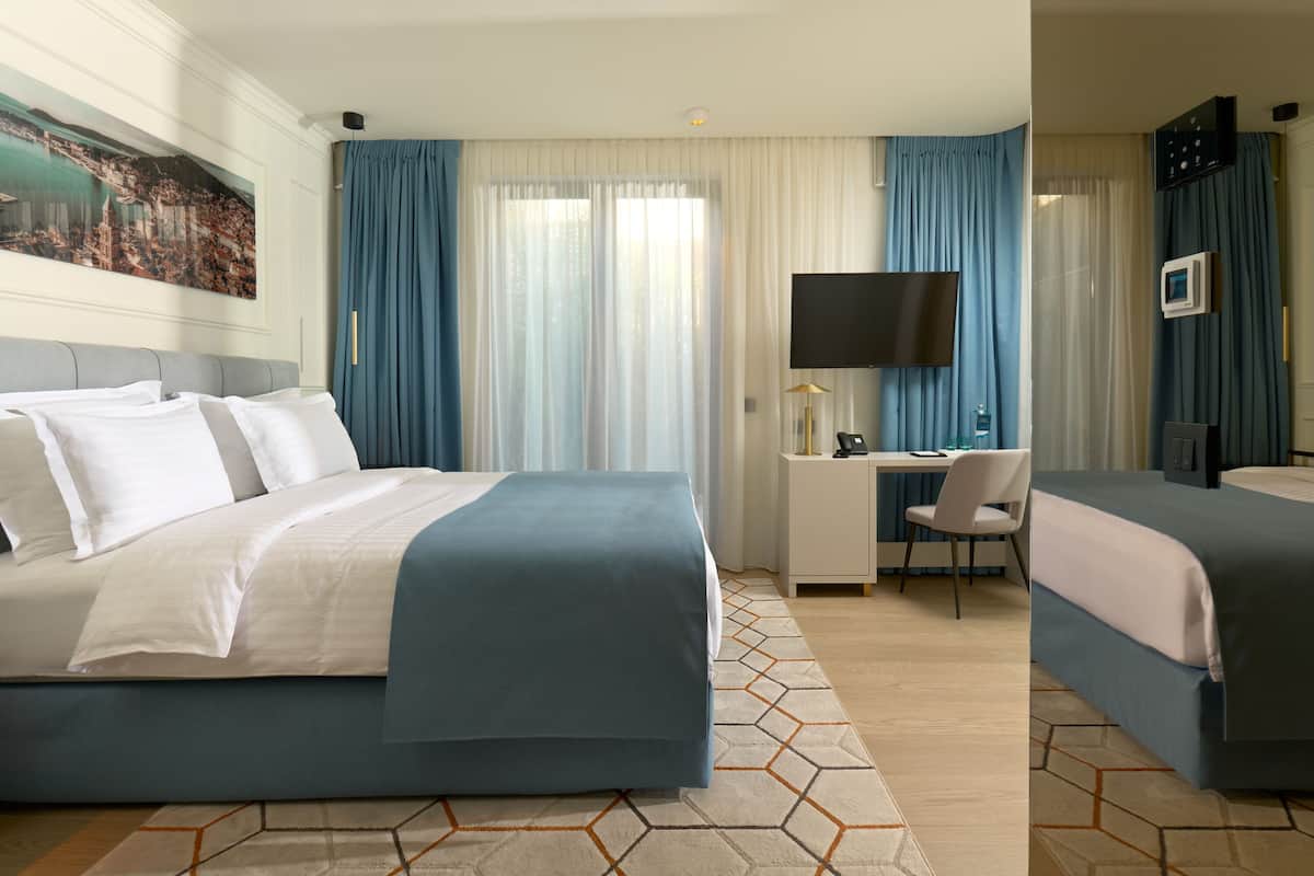 A hotel room with two beds, a desk with a chair, a TV, and a large painting on the wall.