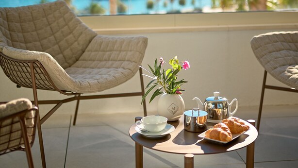 A terrace with wicker chairs, a table with a teapot, cups, and pastries, overlooking a marina and palm trees. - Mirari Boutique Hotel (Split)