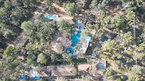 Vue aérienne d’un complexe hôtelier doté de plusieurs piscines, d’une piscine centrale et d’un espace verdoyant environnant.