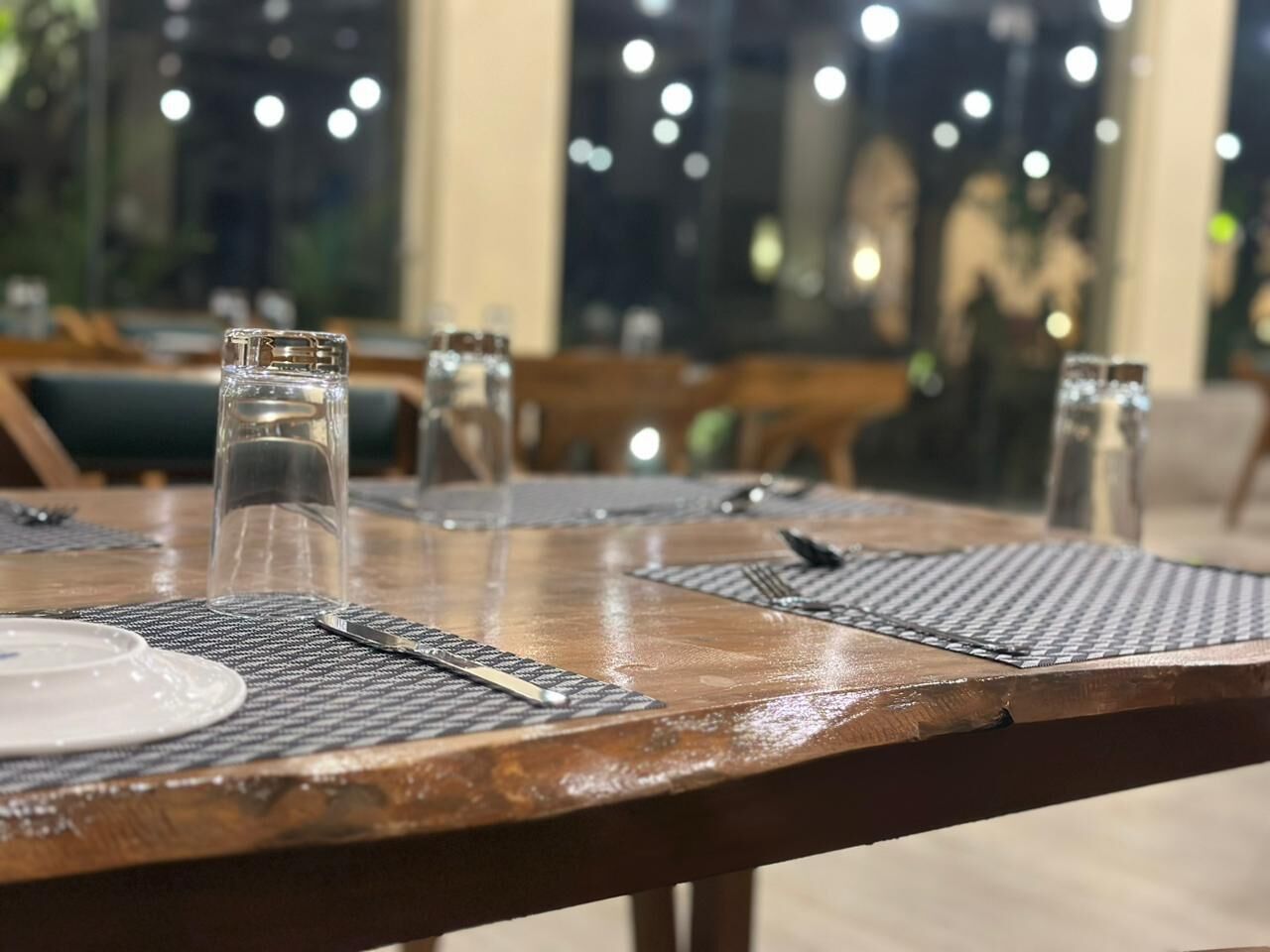 A dining table set with plates, cutlery, and glasses, with a view of the interior and other tables in the background.