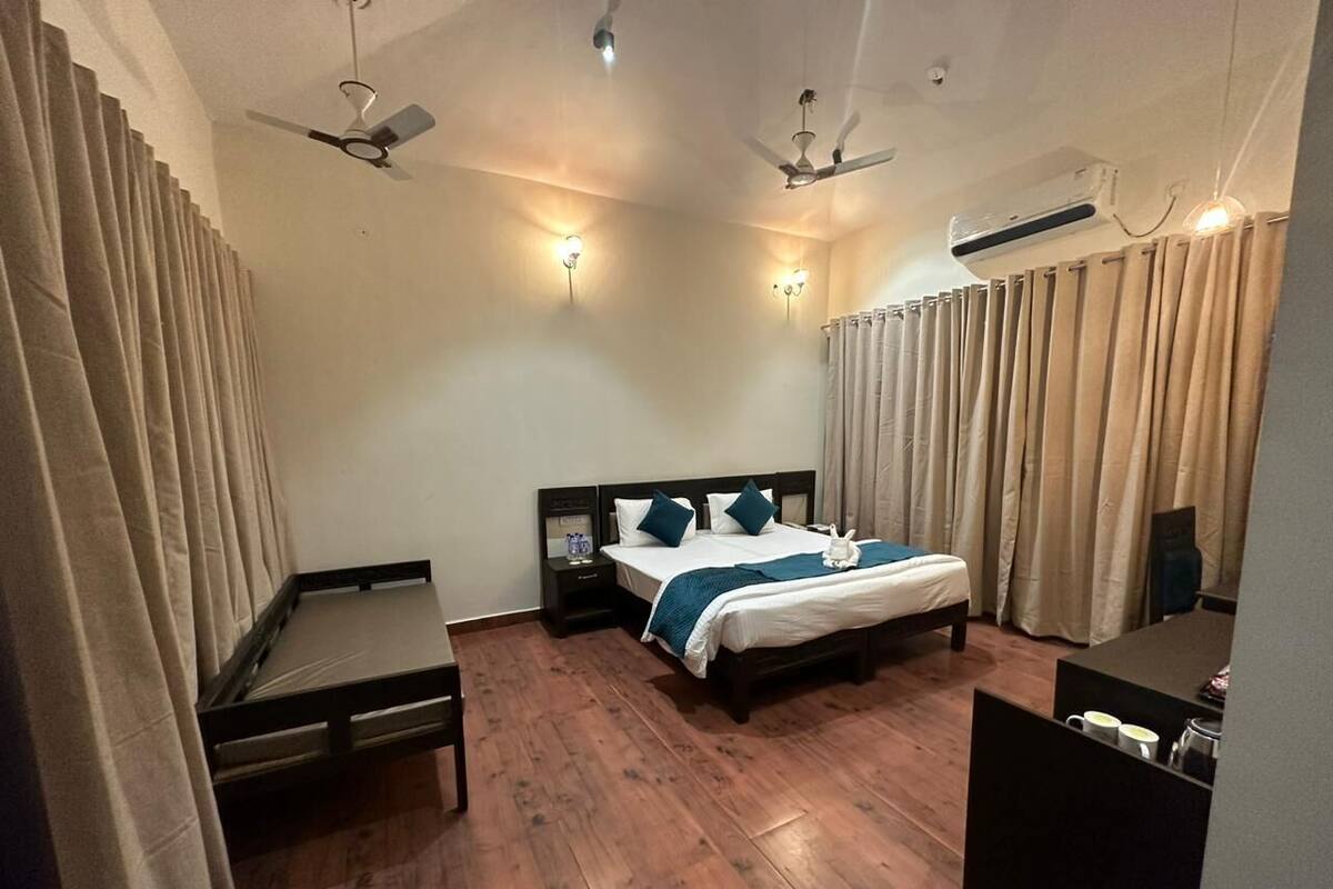 Une chambre d’hôtel comprenant un lit, des tables de chevet, un bureau et une chaise. Elle est équipée de ventilateurs de plafond et d’un appareil de climatisation.