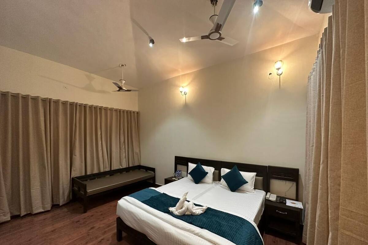 Une chambre d’hôtel avec un grand lit, des tables de chevet, un banc et des ventilateurs de plafond.