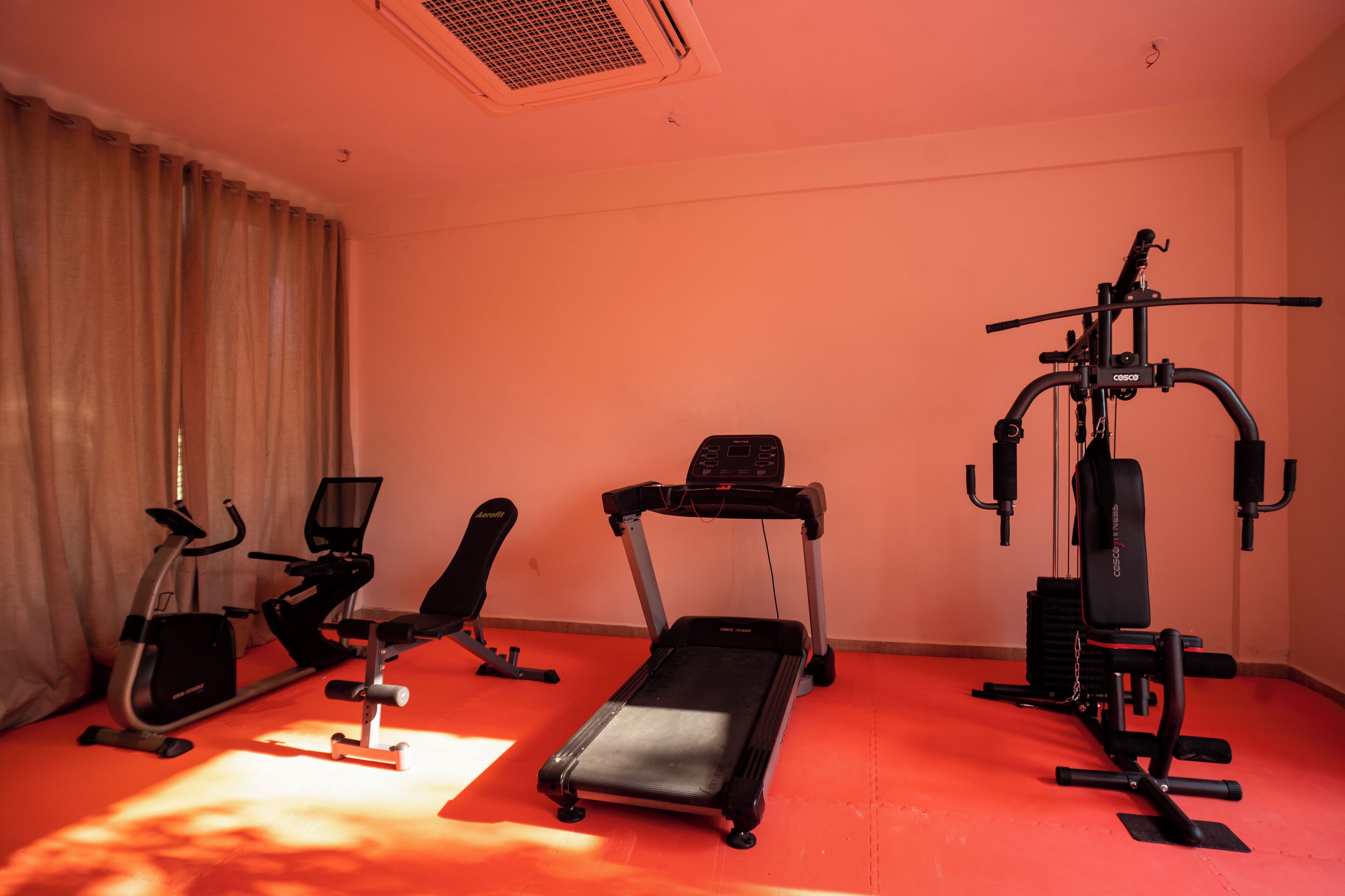 Una habitación con una cinta de correr, bicicleta estática y banco para pesas.