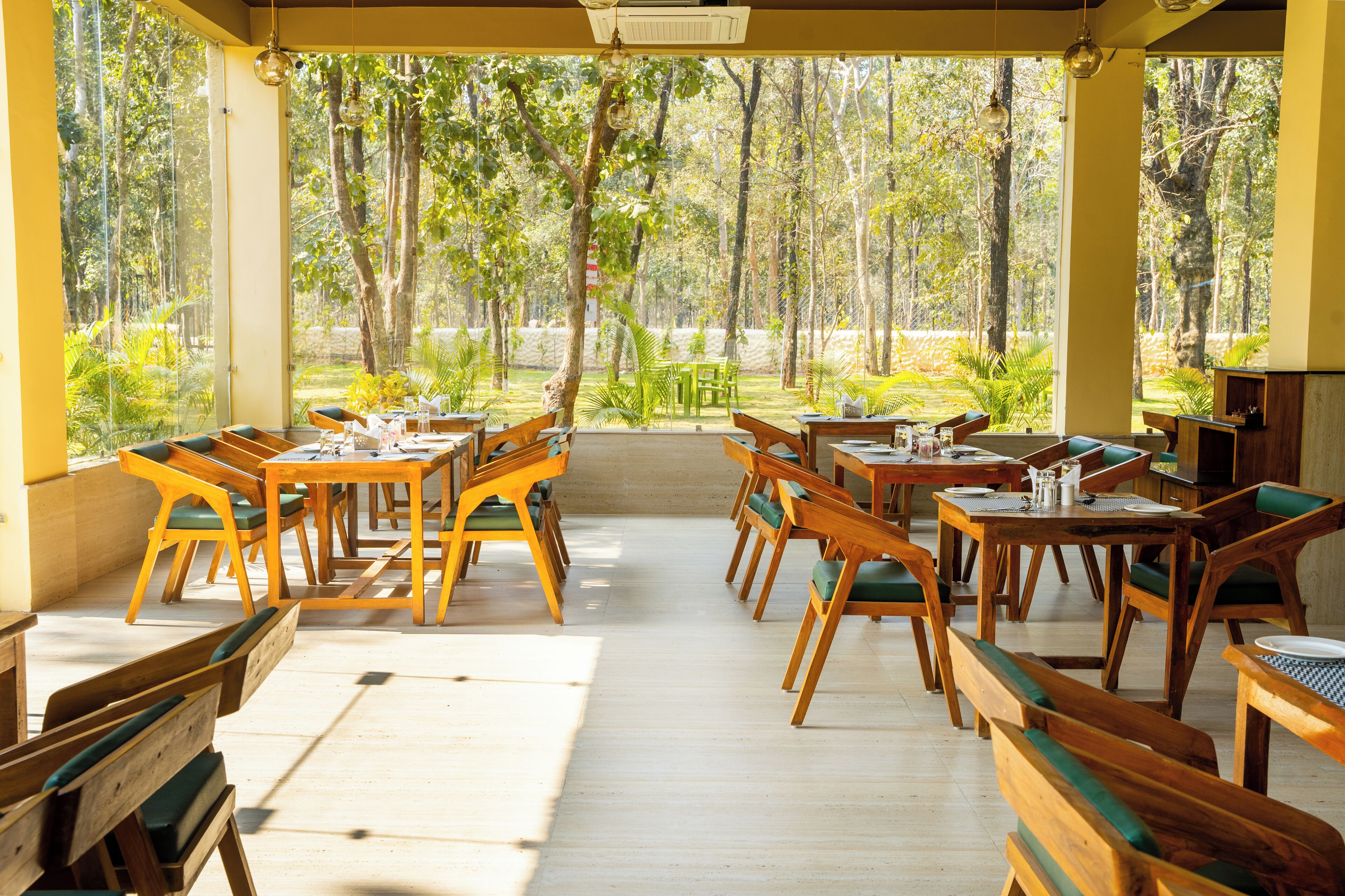 Un área de comedor al aire libre con mesas y sillas de madera, rodeada de vistas al bosque.