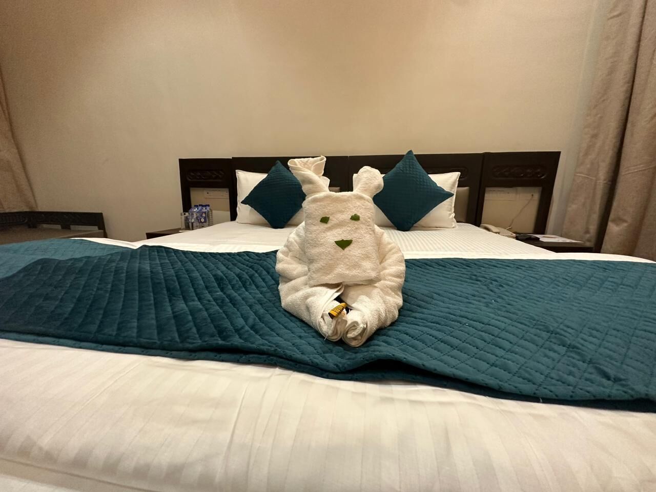 A bed with a teal quilt, a white towel, and two teal pillows.