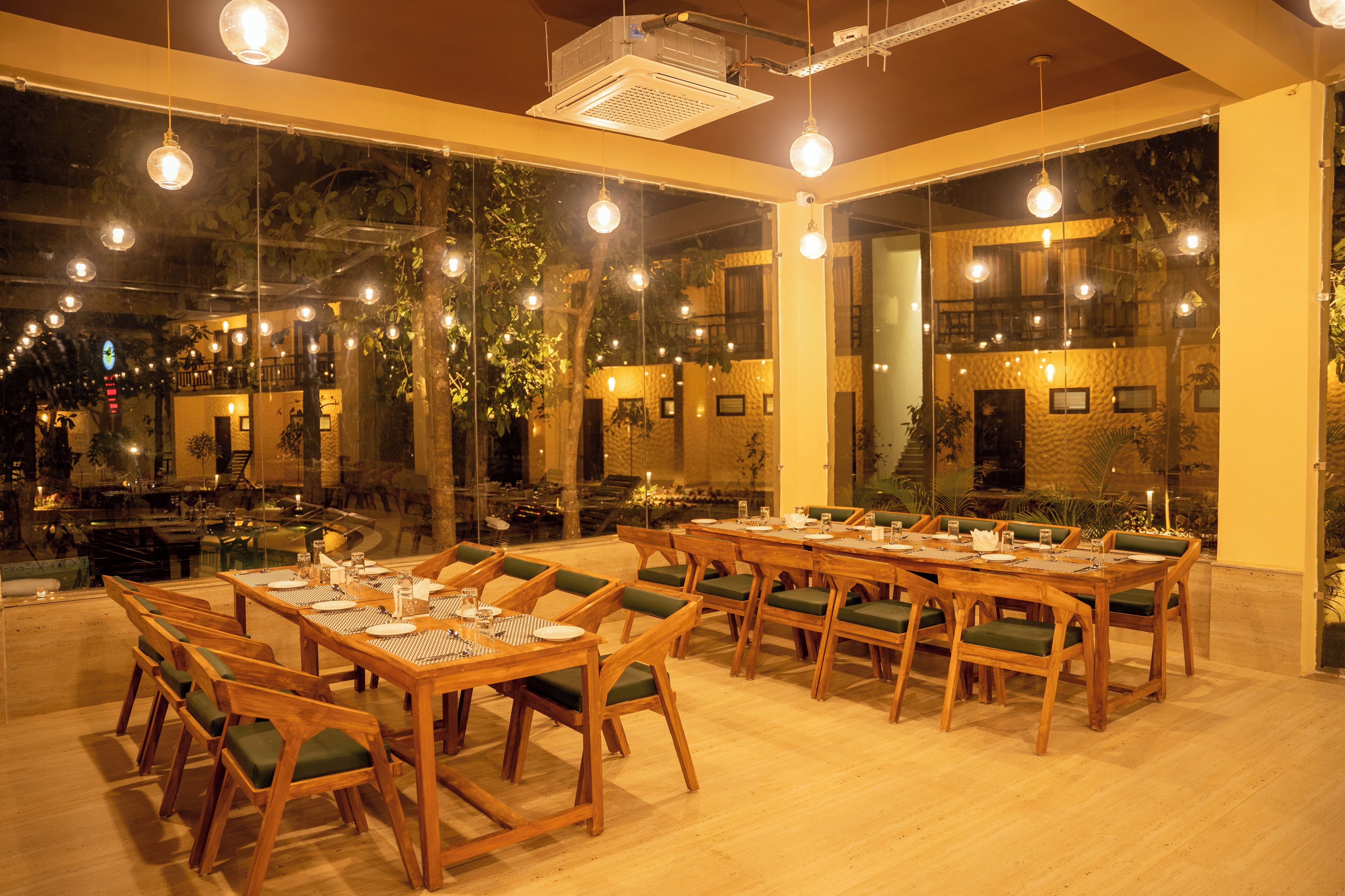 A restaurant with multiple wooden tables and chairs, large windows, and hanging lights.