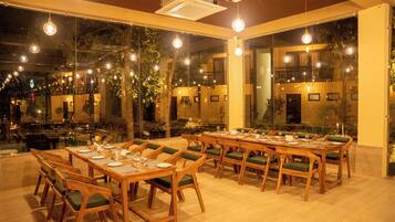 A restaurant with multiple wooden tables and chairs, large windows, and hanging lights.