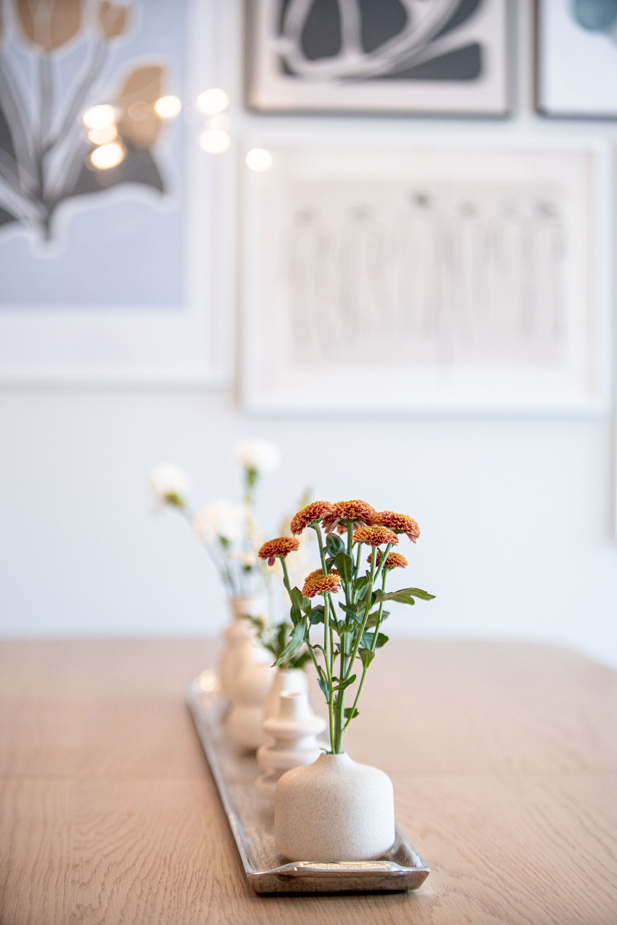 Une rangée de vases remplis de fleurs, disposés sur un plateau, qui se trouve sur une table en bois.