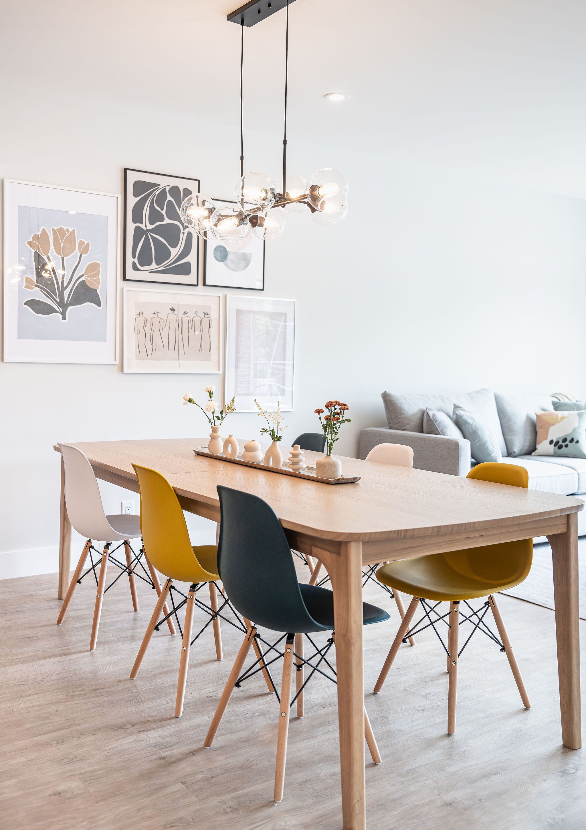 Un espace de salle à manger moderne, avec une table et des chaises en bois, un lustre et des œuvres d’art accrochées au mur.