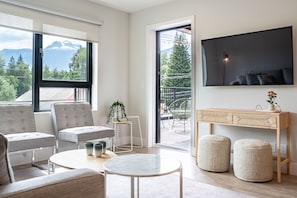 A modern living room with a large window, a flat-screen TV, and a wooden console table. - Western Star by Revelstoke Vacations (Revelstoke)