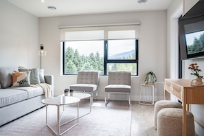 Uma sala de estar moderna com um sofá, duas poltronas, uma mesa de centro e uma TV em um suporte de madeira.