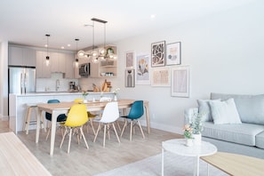 A modern kitchen with white cabinets, a dining area with a wooden table and colorful chairs, and a grey sofa in a living area. - Western Star by Revelstoke Vacations (Revelstoke)
