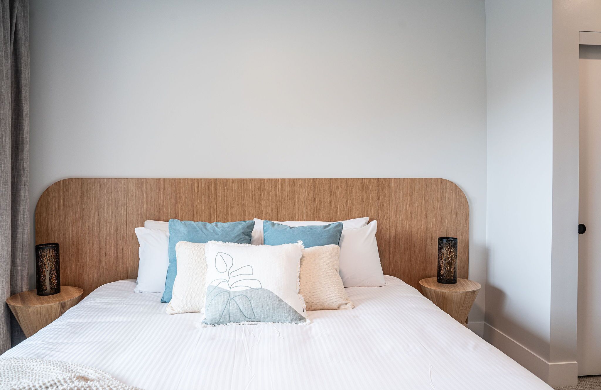 A neatly made bed with a wooden headboard, multiple pillows in various colors, and two bedside tables with decorative vases.