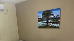 A hotel room with two beds, a painting of a tropical landscape, a white air conditioning unit, and a small table with a remote control. - Pousada Hippocampus (Ipojuca)