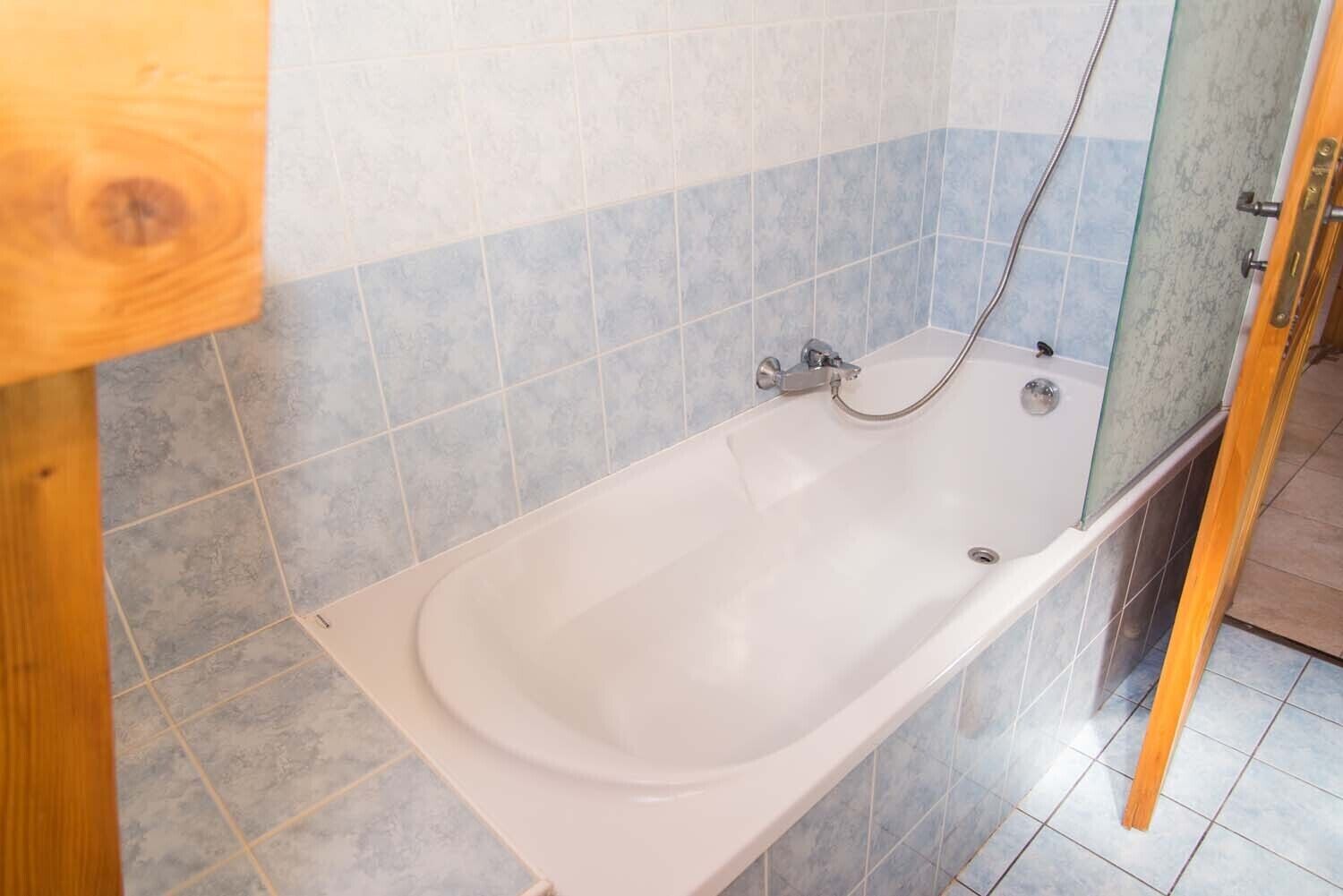 A standard bathtub with a shower head, set against a tiled wall with a blue and white pattern.