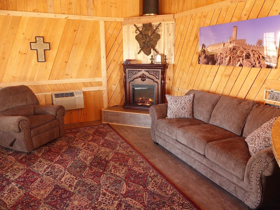 Una sala de estar acogedora con chimenea, paredes de madera, una cruz y un cuadro de un castillo.