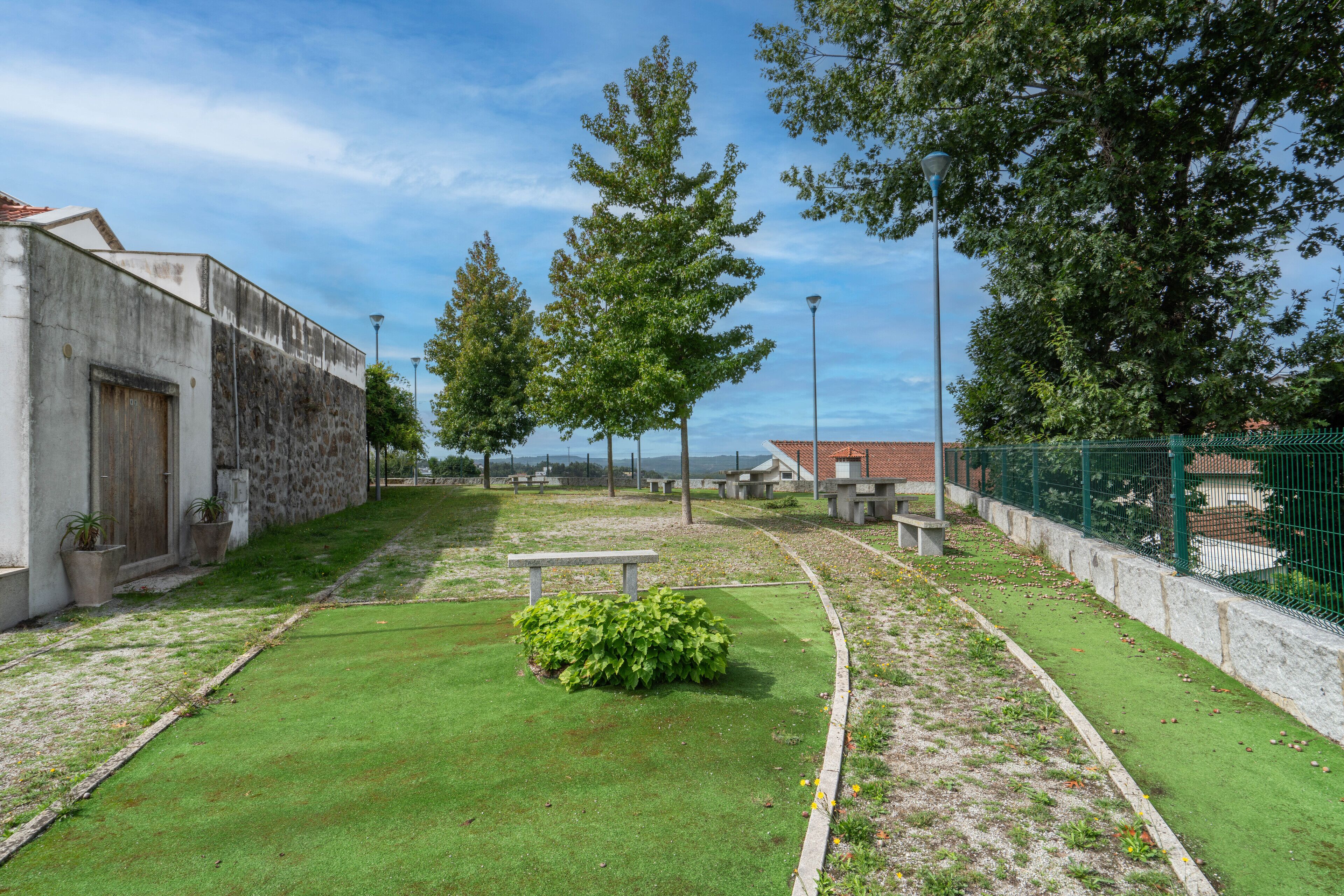 A courtyard with a bench, green lawn, trees, and a stone building.