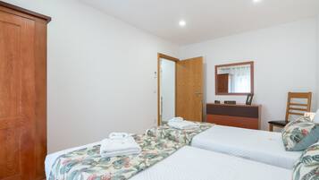 A hotel room with two beds, a wooden wardrobe, a mirror, and a desk with a chair.