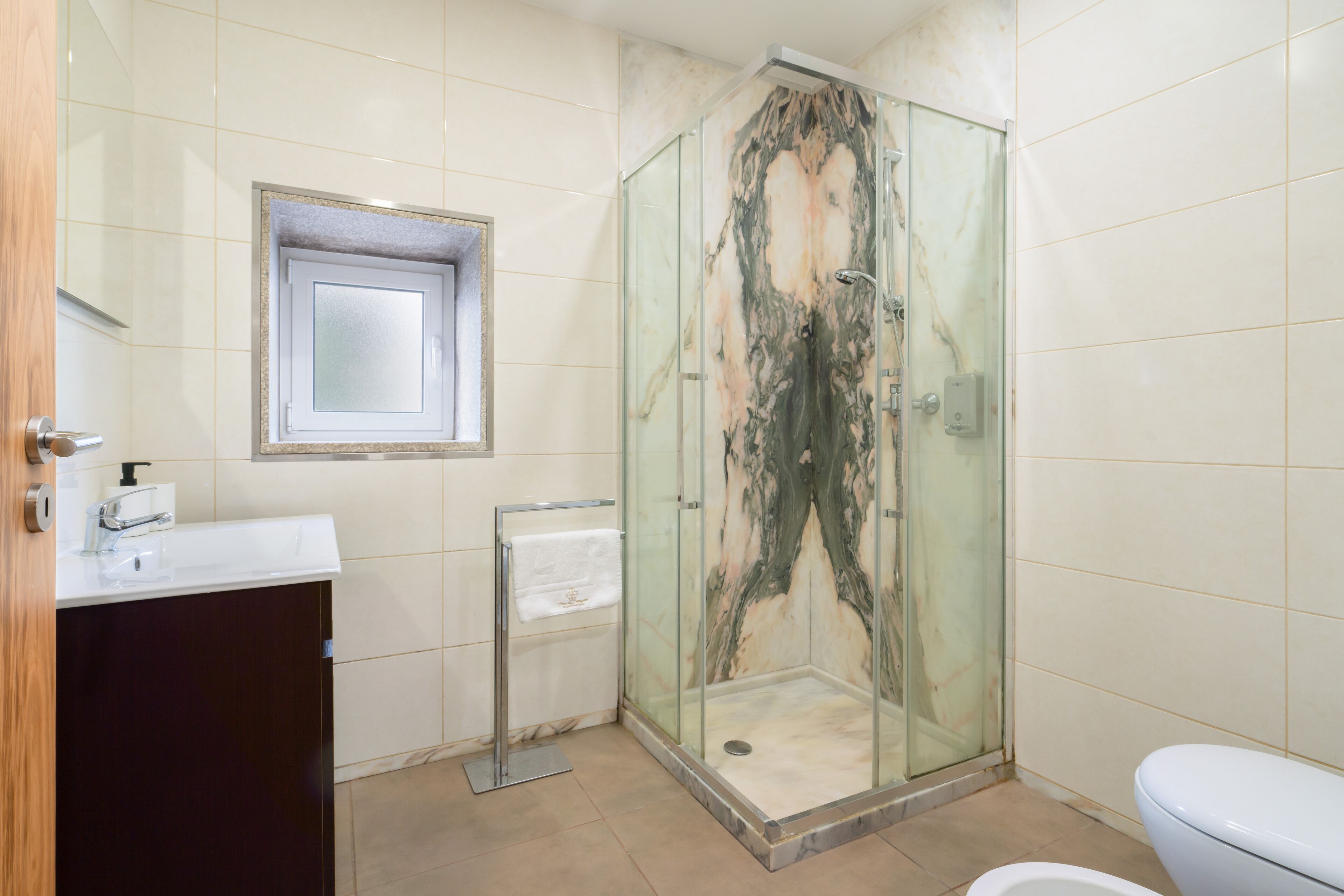 A bathroom with a glass-enclosed shower, a white sink, a mirror, and a toilet.