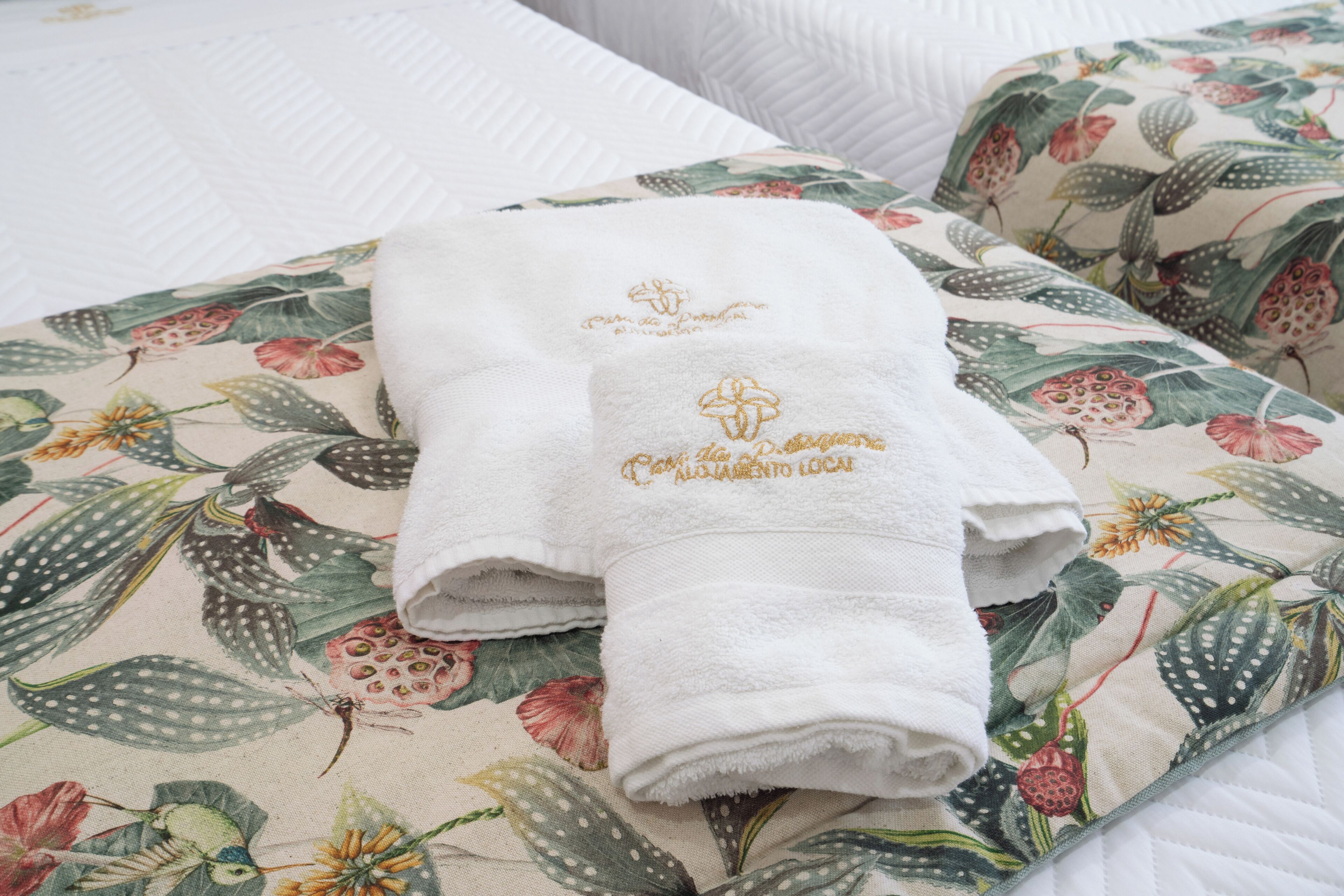 A neatly folded white towel with embroidered text on a floral-patterned bedspread.