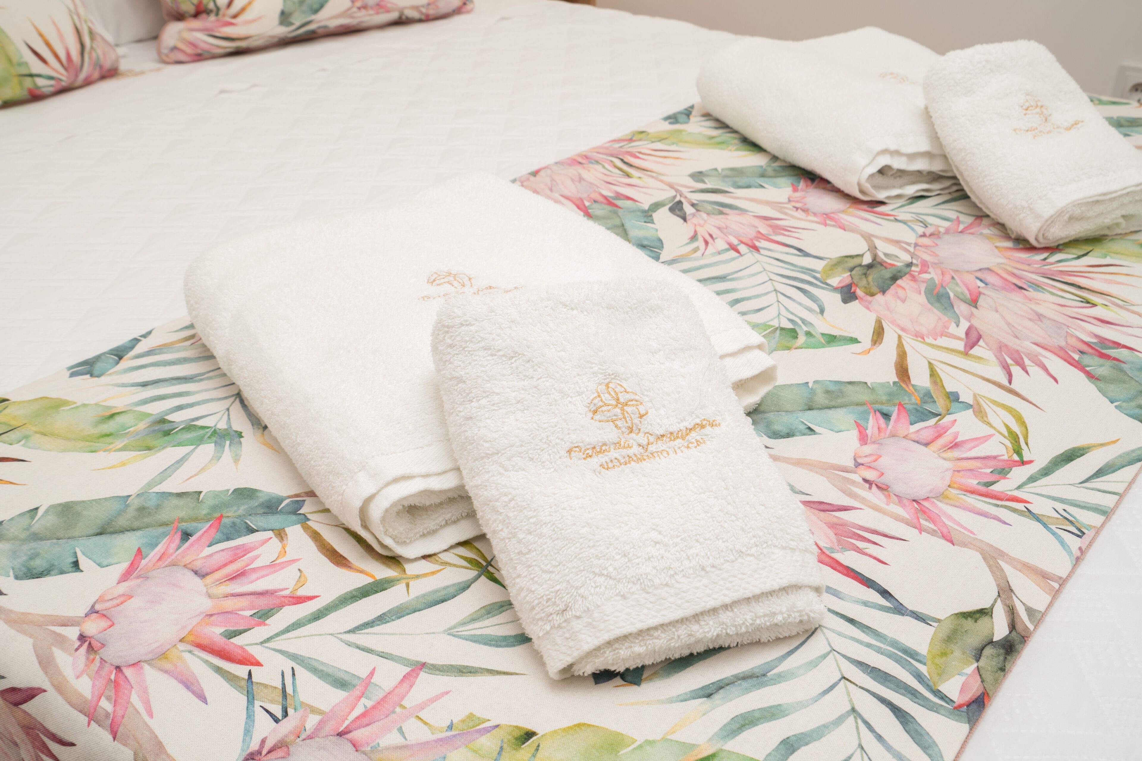 Neatly folded white towels with embroidered text on a bed with a floral-patterned bedspread.