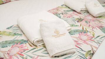 Neatly folded white towels with embroidered text on a bed with a floral-patterned bedspread.