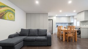 A modern living room with a grey sectional sofa, a dining area with wooden chairs, and a kitchen with white cabinets and a washing machine. - Casas da Petisqueira 61 - Paredes-Oporto (Paredes)