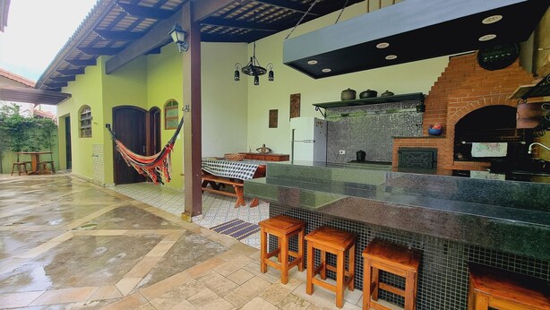Eine Terrasse mit gefliestem Boden, einer Hängematte, einem Tisch mit kariertem Tischläufer und einem Backofen aus Ziegeln.